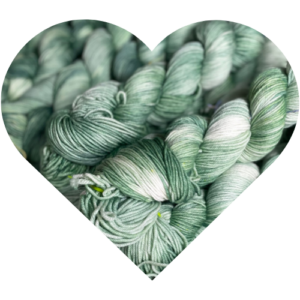 Heart-shaped crop of hand-dyed Stillness yarn skeins in soft green and ivory tones from the Winter Hymn Collection.
