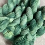 Multiple skeins of hand-dyed green merino yarn arranged together.