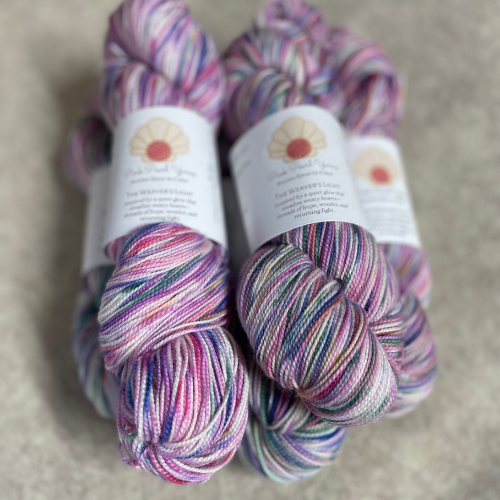 Hand painted fingering weight yarn skeins in The Weaver’s Light colorway, displaying softer blended tones on non-superwash merino wool.