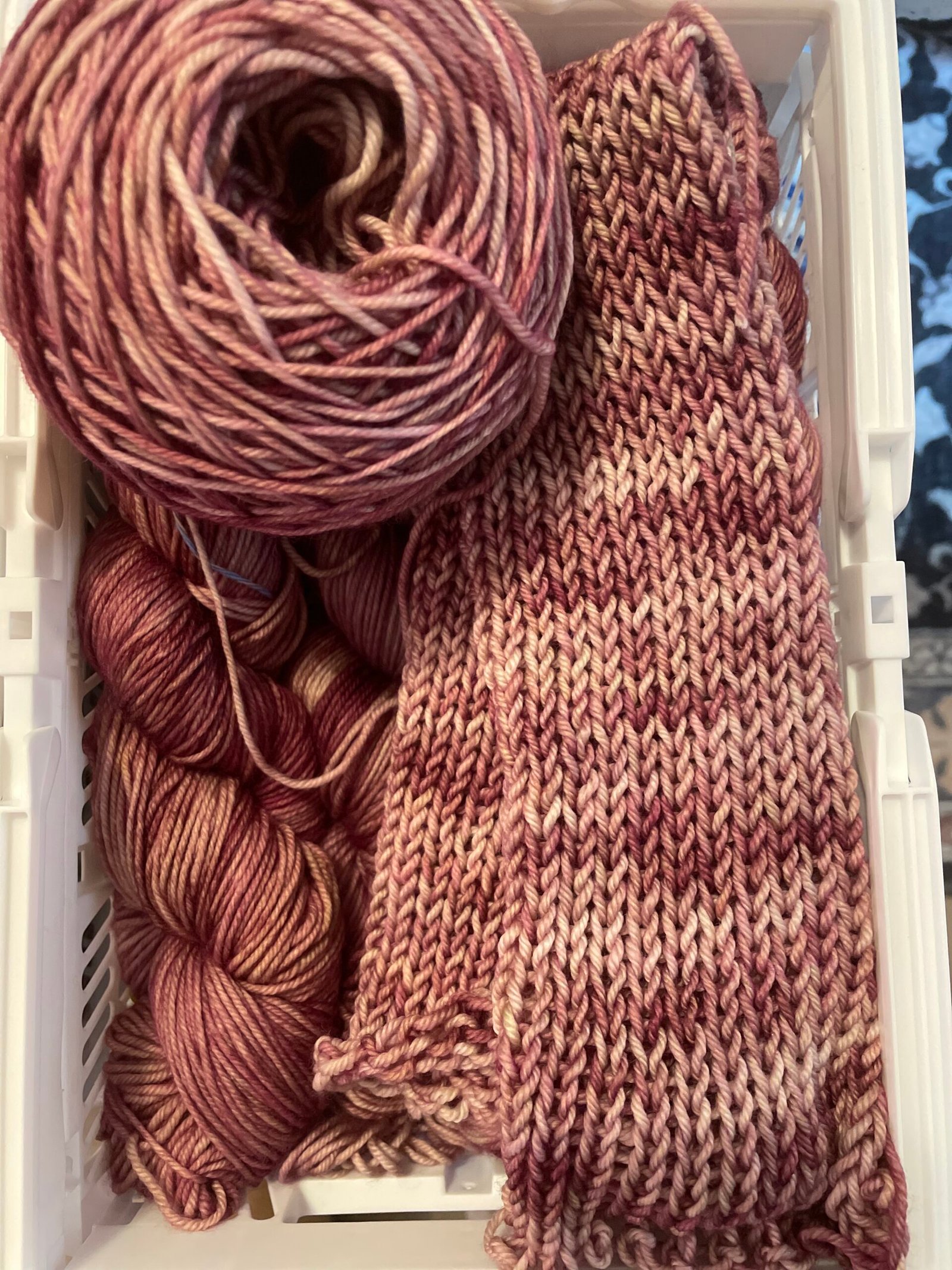 Hand dyed rose clay yarn knit swatch with matching yarn cake and skeins in warm clay and muted berry tones in a basket.