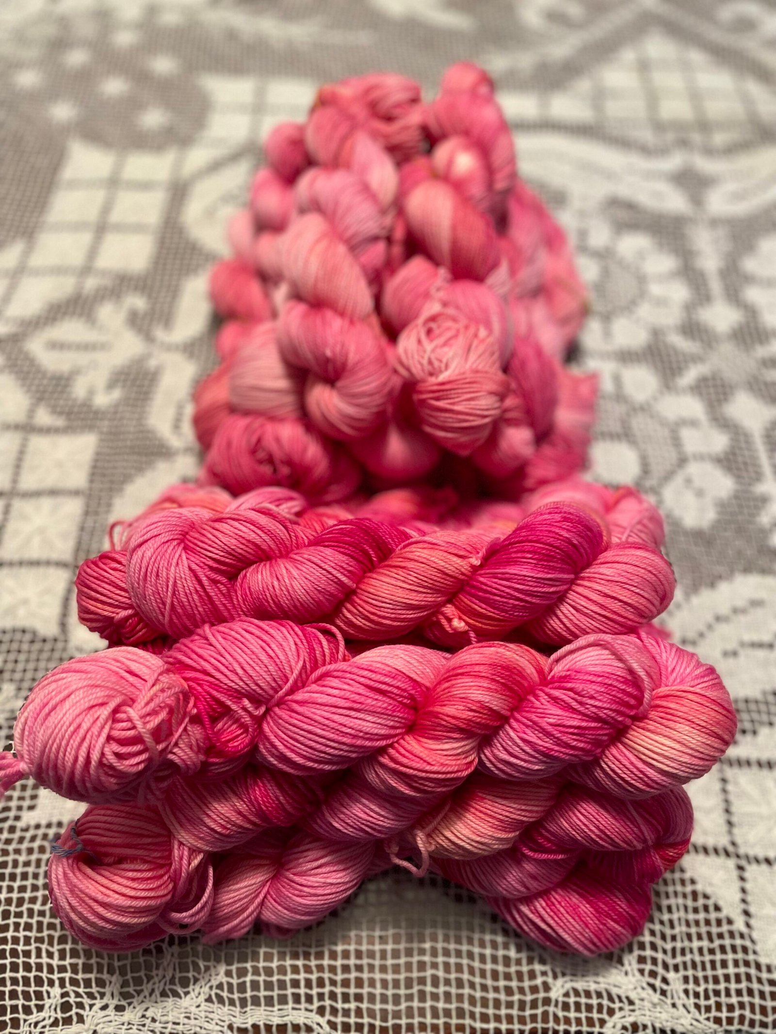 Heart Rest pink hand dyed yarn knit sample beside skein on lace tablecloth. DK in the front Fingering weight yarn in the back.