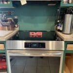New stainless steel induction range installed in a cozy home kitchen with teal walls and baking tools nearby.