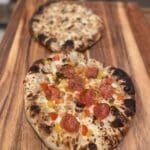 Two homemade pizzas baked on a wooden board with crispy crusts and assorted toppings including pepperoni and cheese.